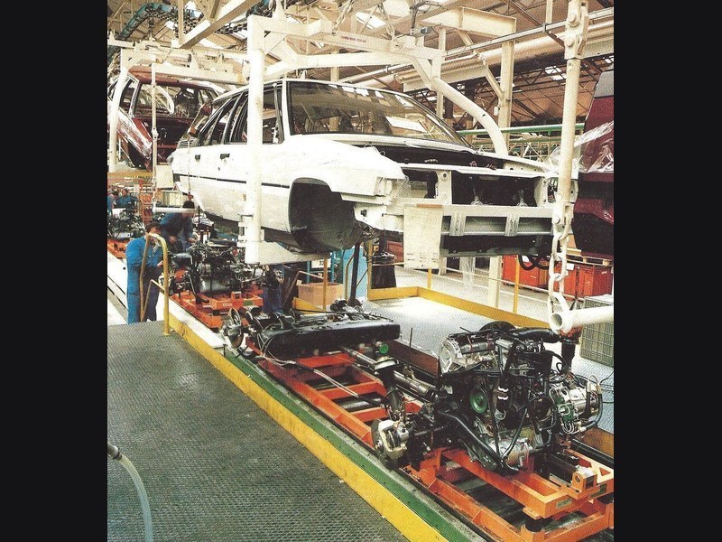Industrial assembly line with overhead conveyor and stationary fixtures
